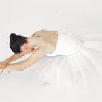 A graceful ballerina in white tutu stretching on a clean white background.