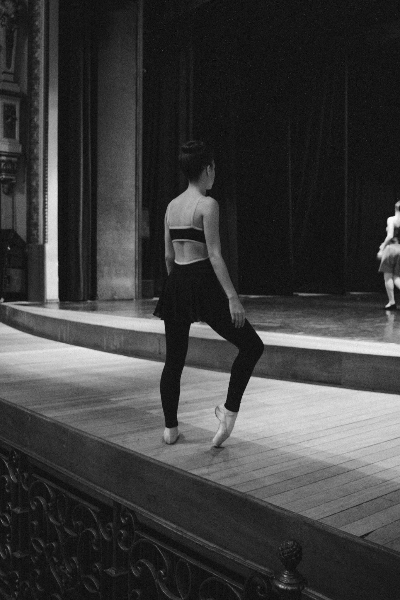 Black and white photo of a ballerina practicing on stage, capturing grace and focus.
