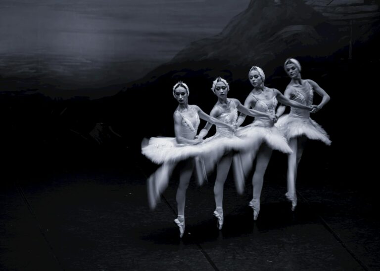 Graceful ballerinas in classic Swan Lake costumes on stage in motion.